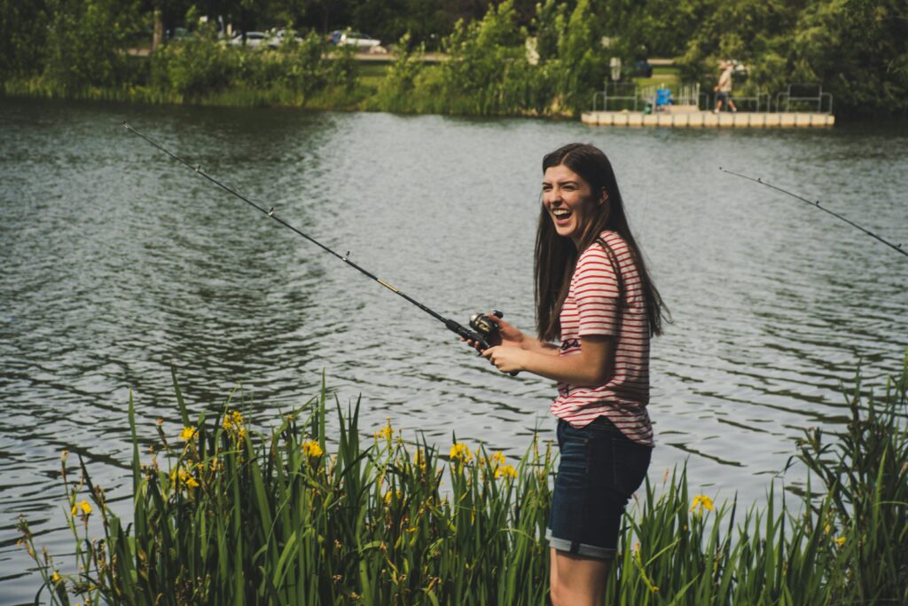 
In the image, a joyful fisherman in Canada is engaged in a leisurely fishing activity. Standing at the edge of a lush, grassy area by a calm lake, the person is dressed in casual outdoor attire suitable for a day of fishing. The backdrop features tranquil waters and a scenic landscape, typical of Canadian natural fishing spots, which enhances the overall serene outdoor experience. The fisherman's laughter and relaxed posture suggest a successful and enjoyable day out in nature, embodying the essence of recreational fishing in Canada.